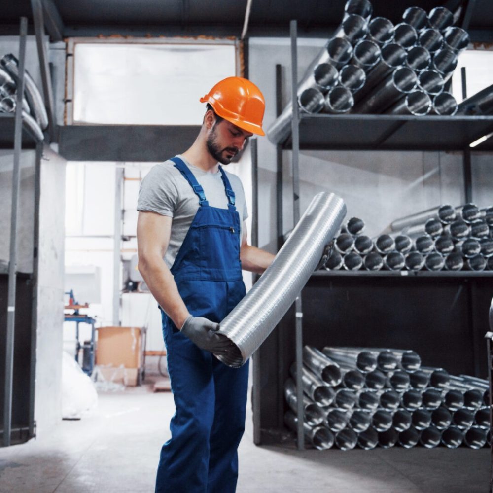 Portrait of a young worker in a hard hat at a large metalworking plant. Shiftman on the warehouse of finished products.